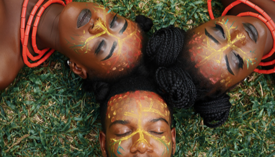 3 jeunes adultes allongés dans l'herbe. ils ont des maquillages ethniques sur le visage. leurs yeux sont fermés. 