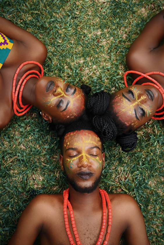 3 jeunes adultes allongés dans l'herbe. ils ont des maquillages ethniques sur le visage. leurs yeux sont fermés. 